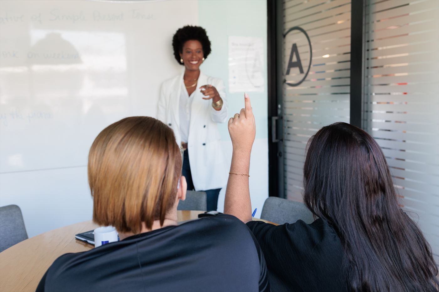 Professora em pé no quadro explicando para a turma, numa sala da empresa