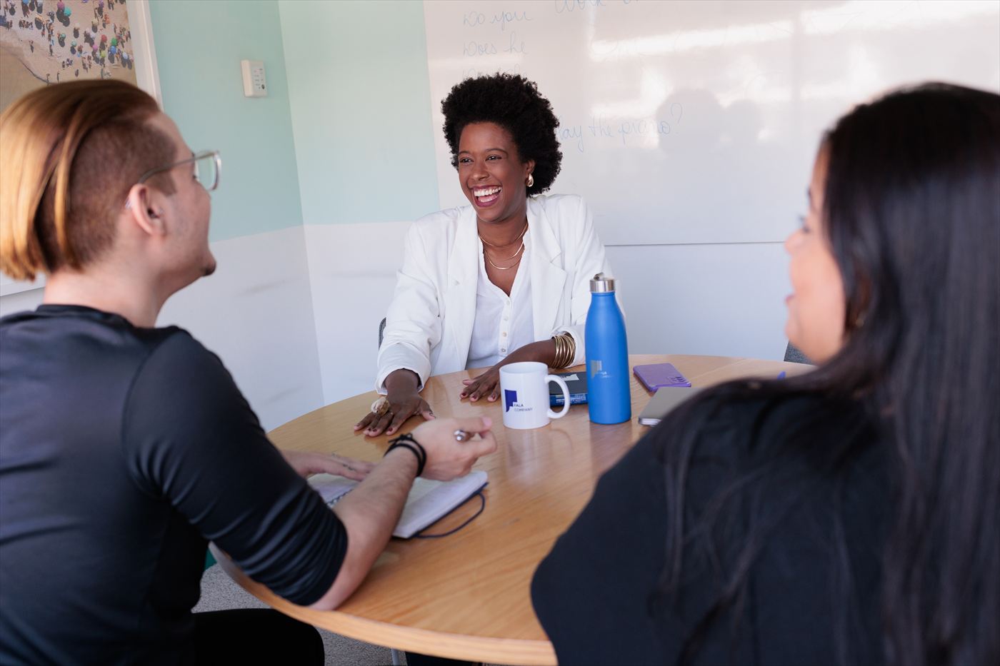 Turma em volta da mesa com a professora, numa sala da empresa