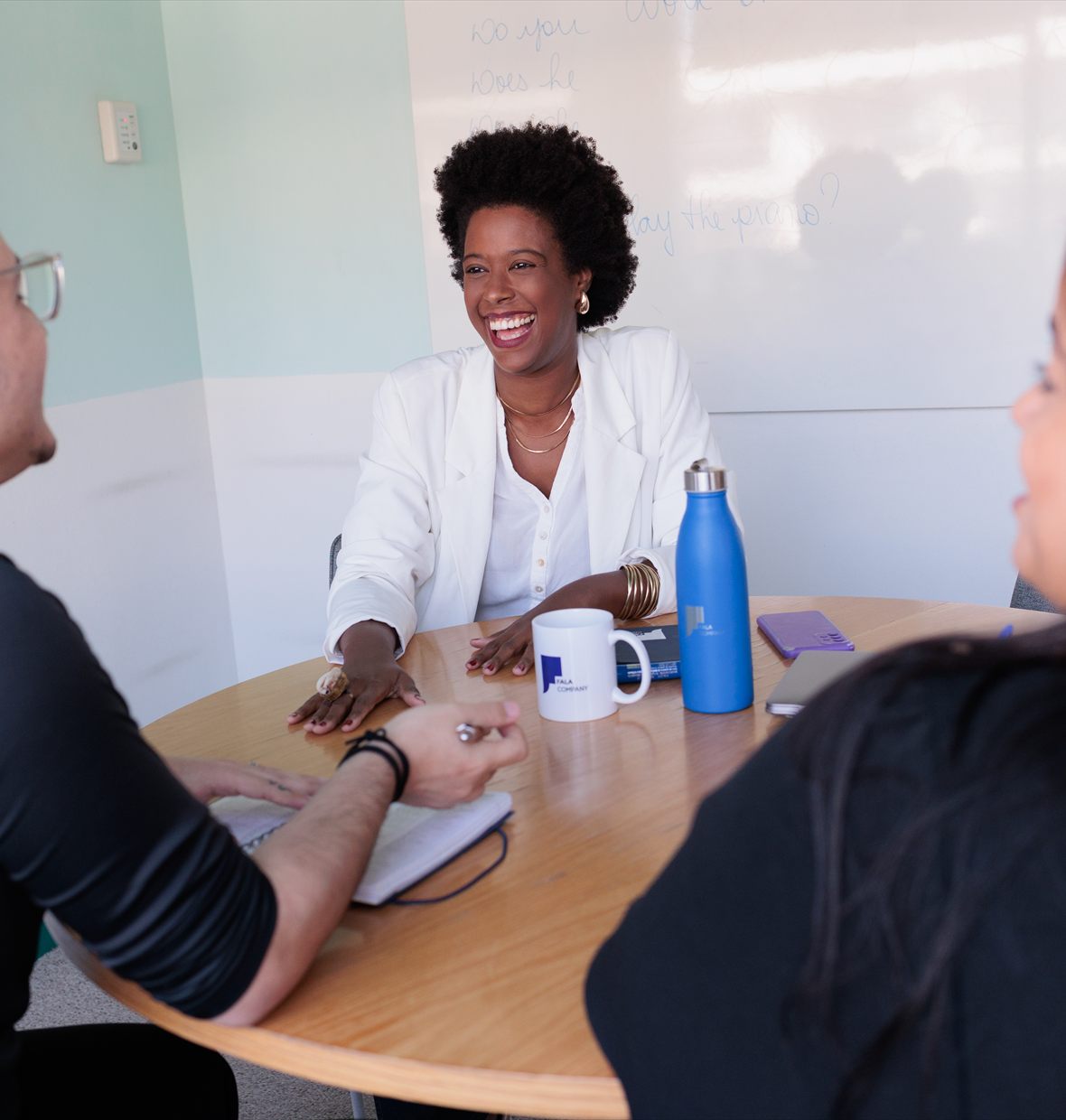 Turma em volta da mesa com a professora, numa sala da empresa